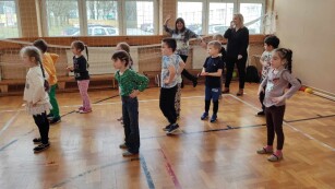 Na sali gimnastycznej grupa dzieci wykonuje ćwiczenia fizyczne.