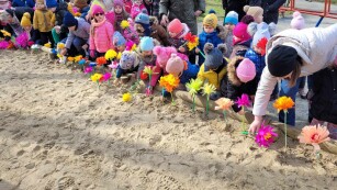 dzieci wkładaja w piasek kolorowe kwiatki z papieru