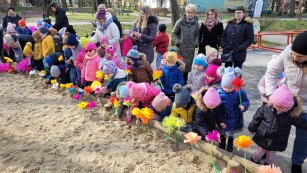 Na placu zabaw radosne dzieci stoją wokół dużej piaskownicy.