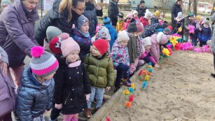 radosne dzieci stoją wokół piaskownicy pełnej kolorowych kwiatów z papieru.