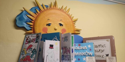 Na pólce z żóltym uśmiechniętym słoneczkeim stoją książeczki wykonane przez dzieci.