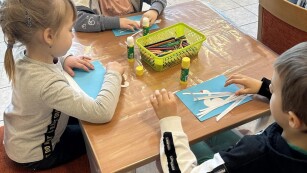dwie dzieczynki i chłopiec siedzą przy stoliku i kleją łabędzia z papieru