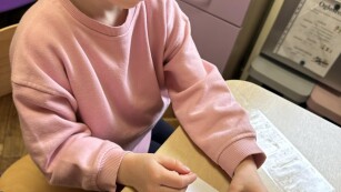 Dzieczynka w różowej bluzce siedzi przy stoliku i lepi zwierzątka z plasteliny