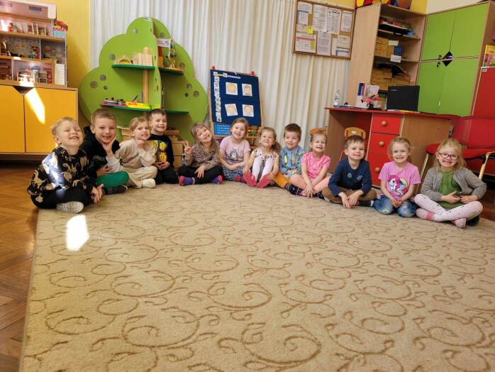 grupa dzieci siedzi na dywanie i szeroko się uśmiecha