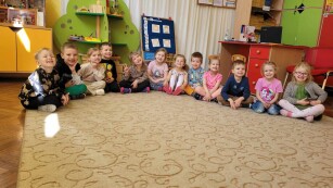 grupa dzieci siedzi na dywanie i szeroko się uśmiecha